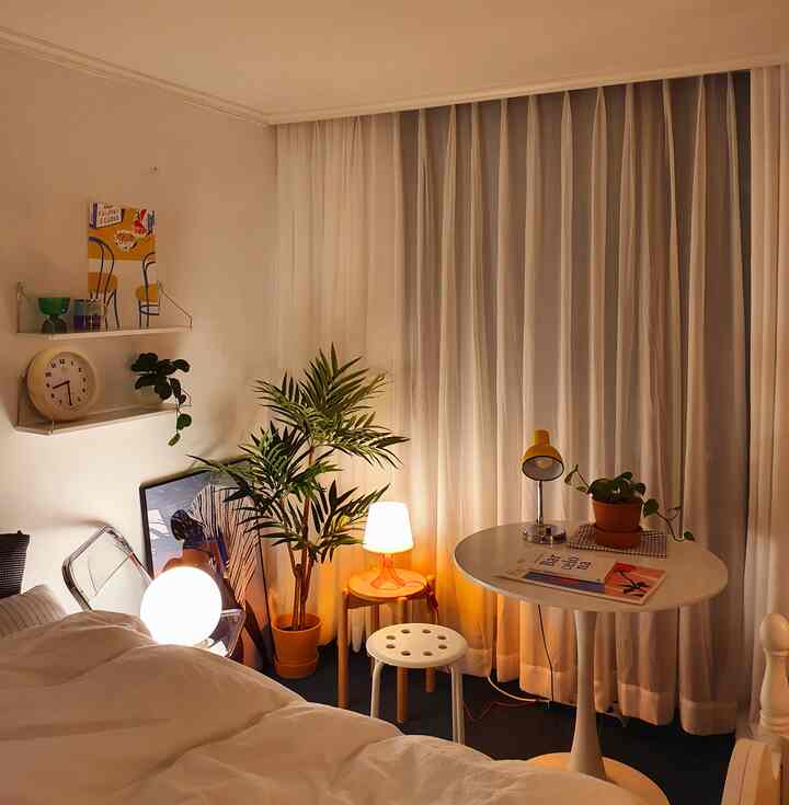 Warm white and brown toned bedroom featuring round table, ambient lamps, and plants creating a cozy atmosphere