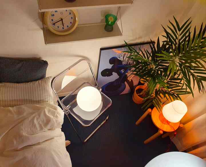 Small bedroom with blue flooring and wood tones, featuring transparent stool and table lamp creating cozy ambiance