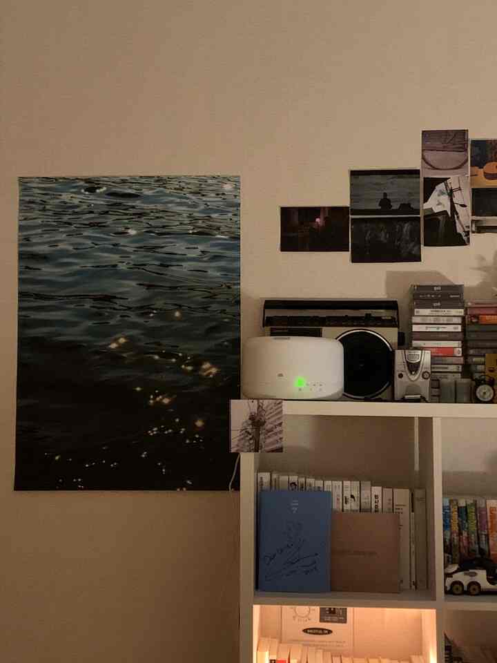 Beige-toned wall with a poster and white bookshelf arranged in a cozy compact room interior