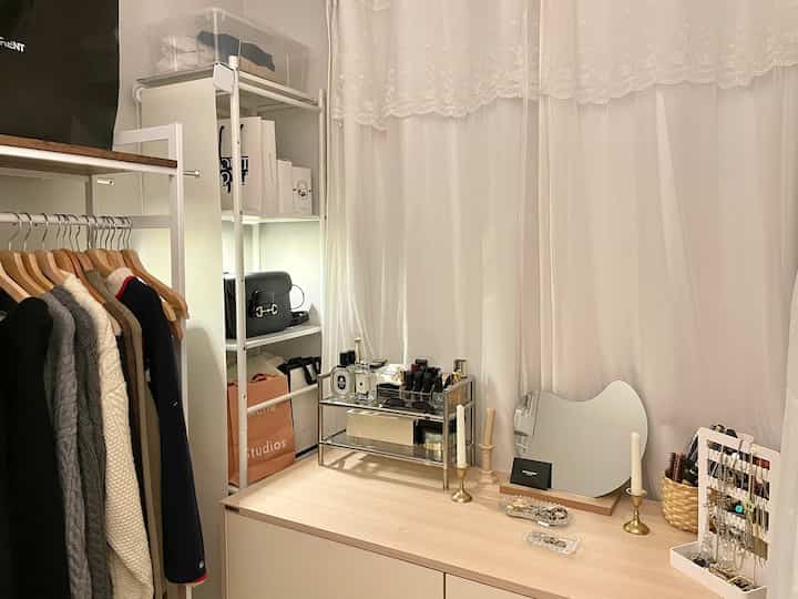 ホワイトとベージュの色調のウォークインクローゼット、棚と化粧台にアクセサリーが配置された落ち着いた空間