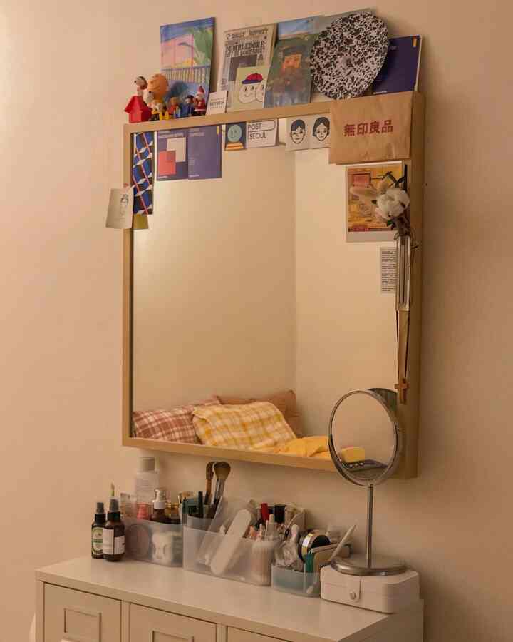 White and natural toned vanity with wall mirror decorated by postcards and objets, creating a cozy space
