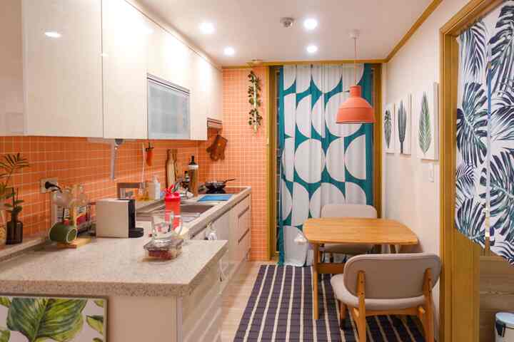 Compact natural single-wall kitchen featuring coral orange tiles, wooden dining table, and pendant light