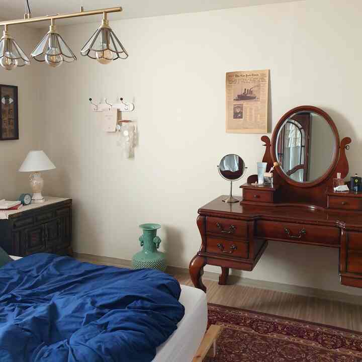 White-walled bedroom with wood-tone antique furniture, featuring blue duvet cover and vanity mirror creating a warm atmosphere