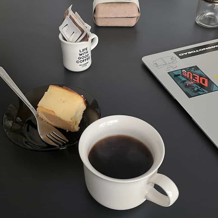 Black table featuring coffee cup, cake, and laptop creating a simple home cafe and work space