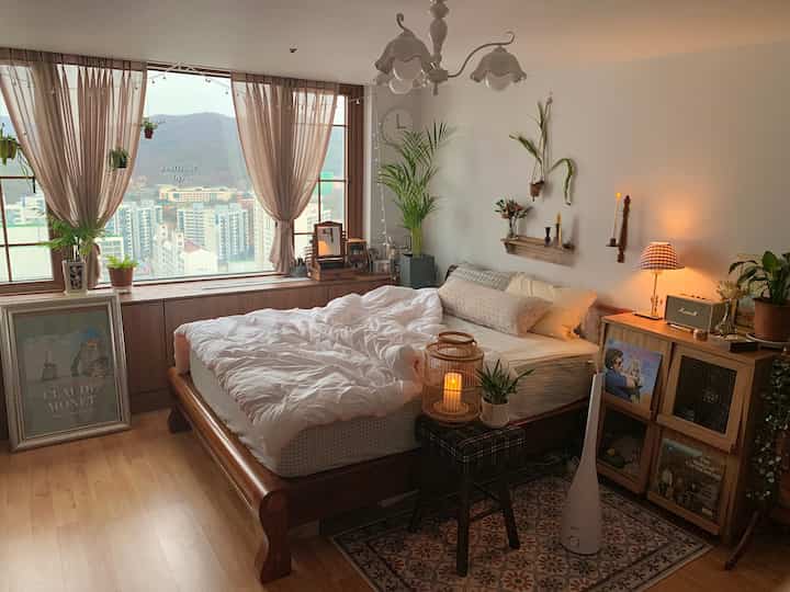 Natural brown and white toned bedroom featuring a wooden bed, nightstand, and plants, creating a warm and cozy atmosphere