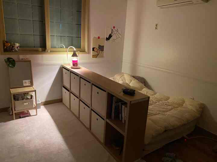 ホワイトと木目調が調和した狭いワンルーム寝室、中央に長い収納棚が配置されたシンプルでナチュラルな空間