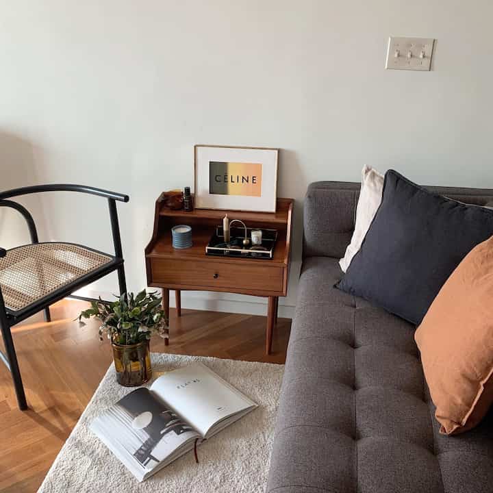 A living room in brown and gray tones featuring a gray sofa, wooden side table, white rug, and cushions creating a cozy atmosphere