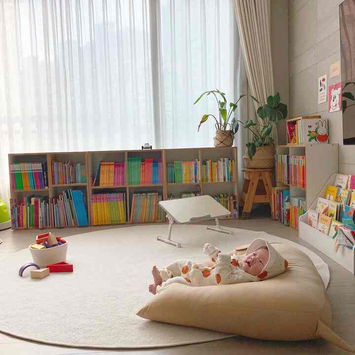 明るいベージュと白の色調の子供部屋、大きな円形のカーペットとカラフルな本棚が配置された、居心地の良い自然な雰囲気のインテリア