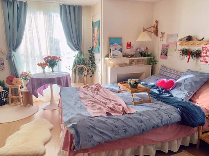 Soft blue and pink toned bedroom with a small table near window and wooden furniture arranged in a cozy setting