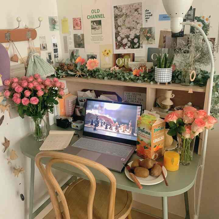 Cozy home office space featuring a light green desk and wooden chair, decorated with vases, plants, laptop, and fruit on the desk