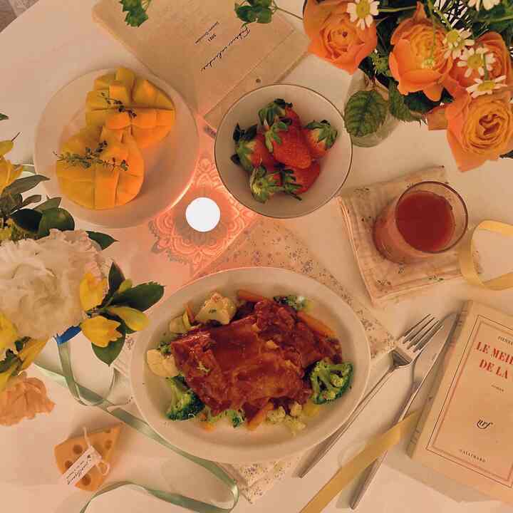 Warm brown and ivory toned dining table featuring barbecue ribs, fruits, candle, and flower vase creating a cozy home party atmosphere