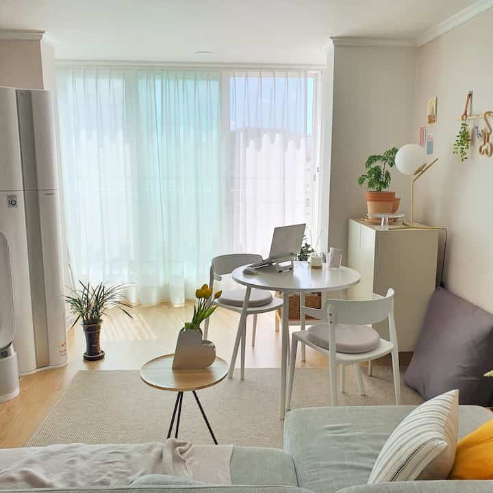 白とベージュのトーンが映えるコンパクトなリビング、丸テーブルと椅子、植物が配置された自然な雰囲気のインテリア