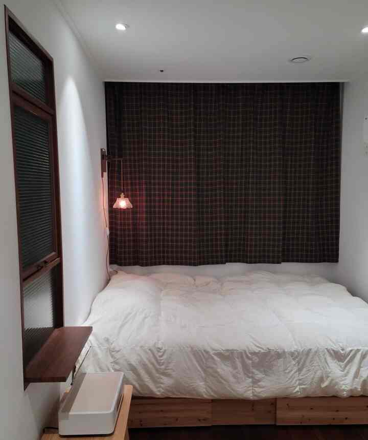White and brown toned bedroom featuring check curtains and wall sconce in a cozy compact space