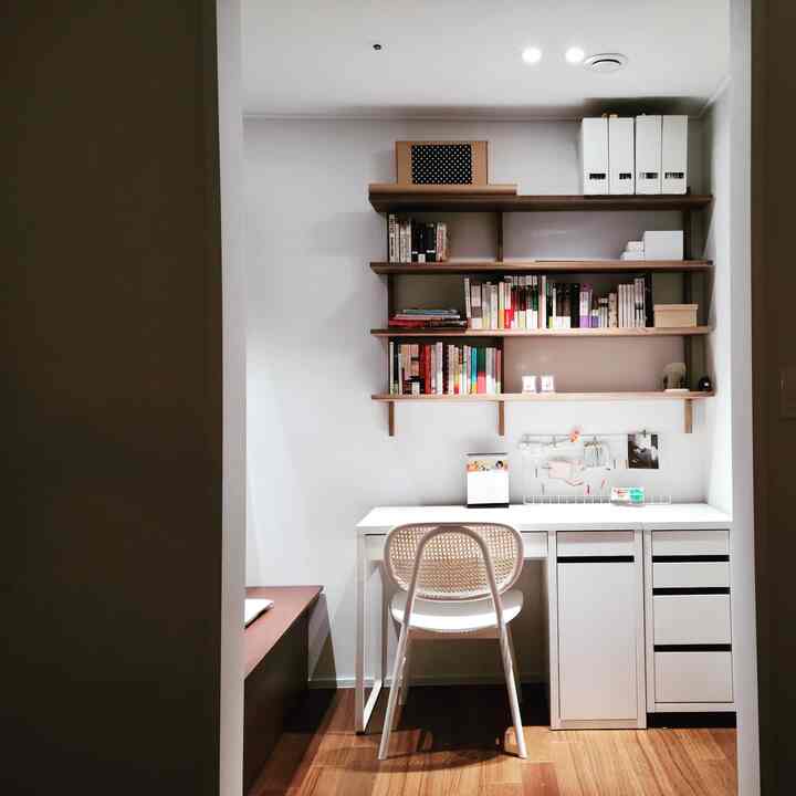 A small study space in natural wood tones and white, featuring a desk and walnut shelves with an organized and neat atmosphere