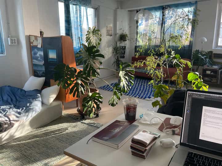 A natural modern workspace in white and blue tones featuring plants, a sofa, and a desk in a cozy arrangement
