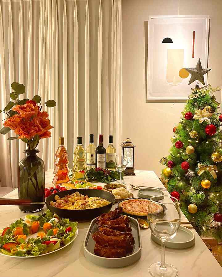 White-toned dining room with Christmas tree, featuring a table richly set with food and drinks for a cozy home party