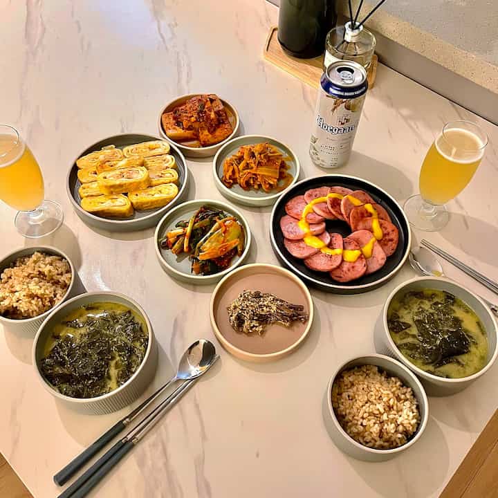 Natural-tone dining table featuring Korean side dishes and drinks set for two, creating a cozy home cafe atmosphere