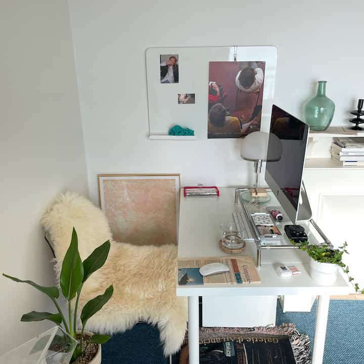 Modern home office in white and blue tones featuring a white desk, armchair with wool throw, and plants creating a clean workspace