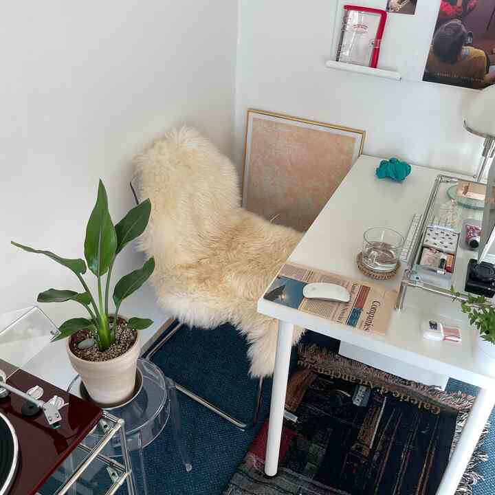 A cozy home cafe space with white walls and desk, a fluffy chair cover, and blue rugs on the floor