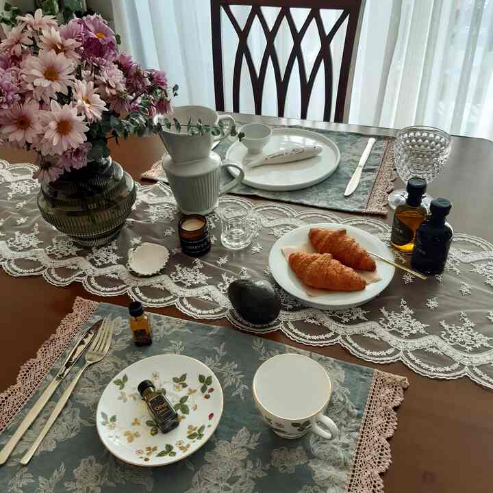 Vintage toned wood dining room featuring lace tablecloth, flowers, and dishes arranged for a cozy breakfast setting