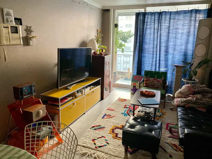 青いカーテンと黄色いテレビ台が配置された、ヴィンテージ家具が印象的な居心地の良いリビング