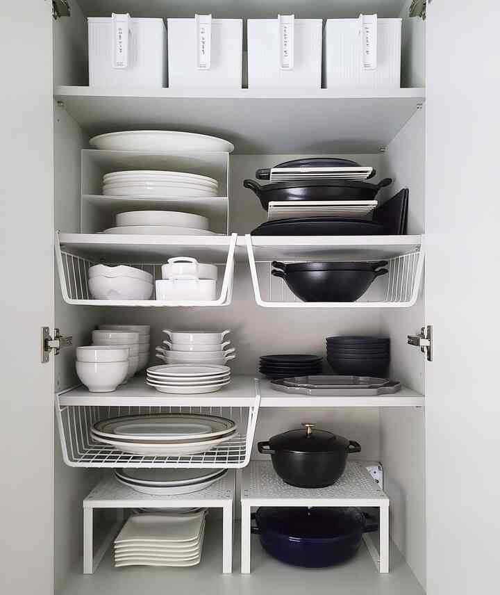 White-toned kitchen dish cabinet neatly organized with plates and pots in a clean storage space