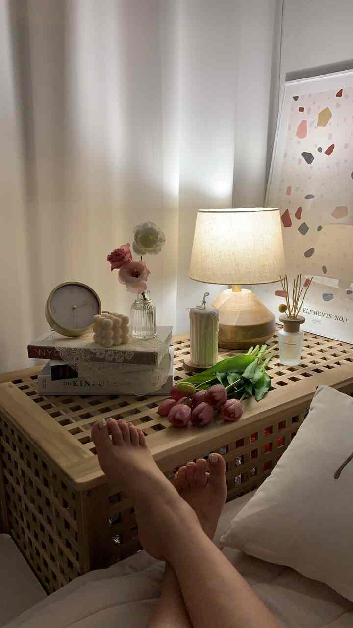 Natural-toned bedroom with wooden side table featuring candles, diffuser, and pink tulip artificial flowers creating a cozy atmosphere