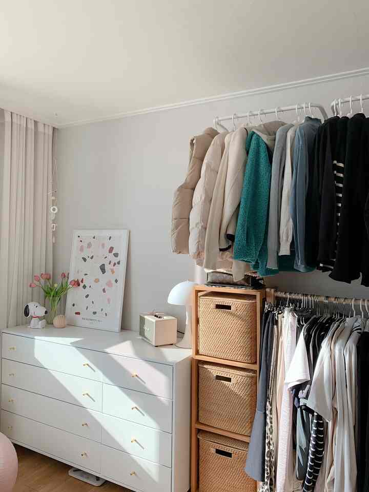 ホワイトとブラウン調のクローゼット空間、ラタン収納キャビネットと壁掛け洋服掛けが調和した清潔でナチュラルなインテリア