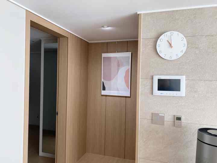 木目調とベージュの調和が取れた玄関、壁時計と抽象画が配置されたシンプルな空間