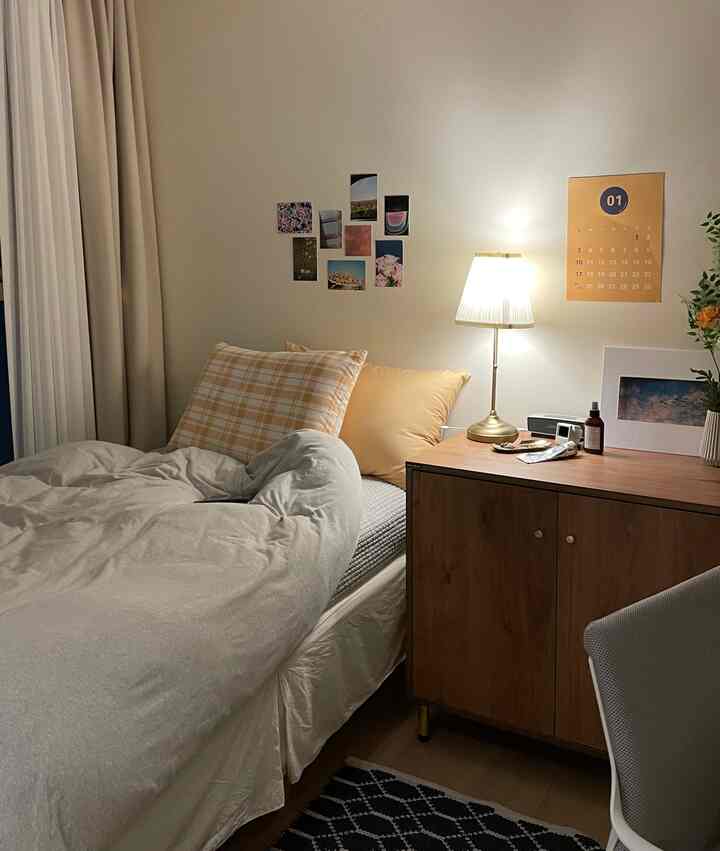 Studio apartment bedroom in white and wood tones featuring a cozy bed, storage cabinet, and soft lighting for a stylish ambiance