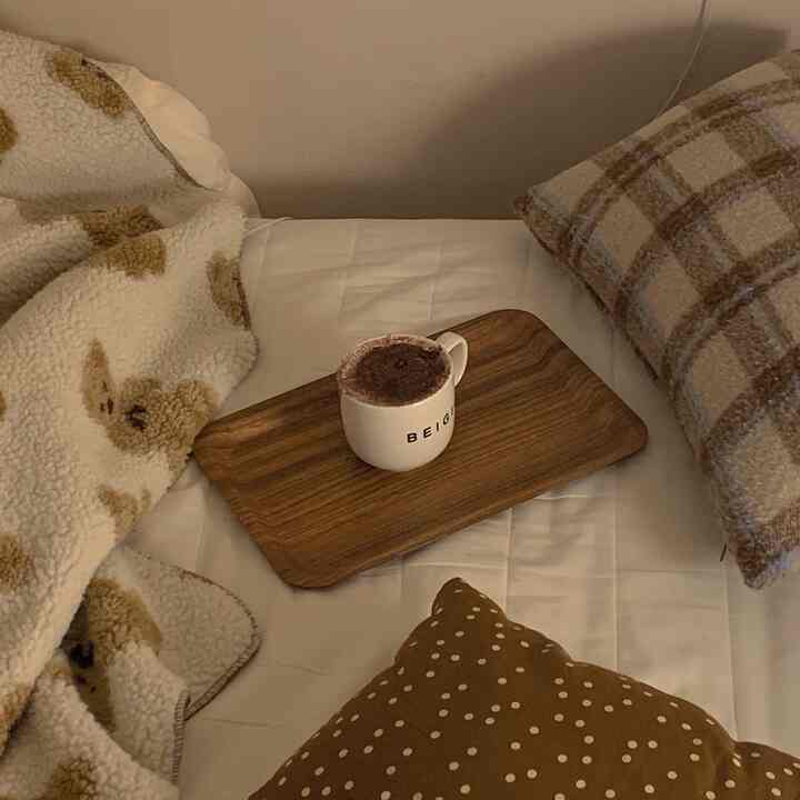 温かみのあるベージュと白の寝室、木製トレイと柔らかいブランケットが配置された雰囲気のあるインテリア