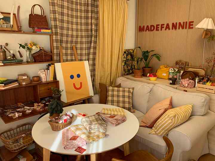 Cozy living room in yellow and natural tones, featuring a beige sofa and white round dining table with various plaid cushions and linens