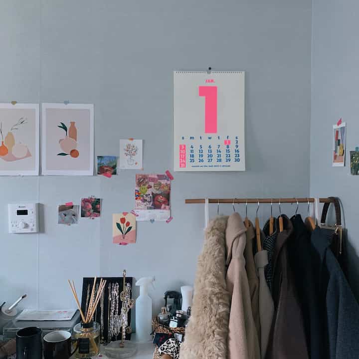 Natural tone small room wall featuring Afrocat monthly calendar, various wall decor, and a clothes rack with coats