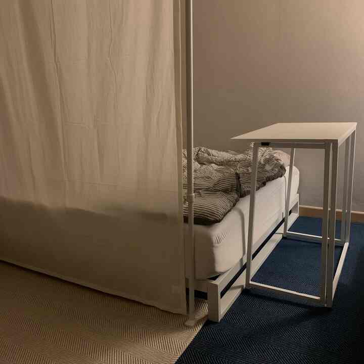 A white and navy toned bedroom featuring a folding side table beside the bed and beige partition curtain creating a cozy atmosphere