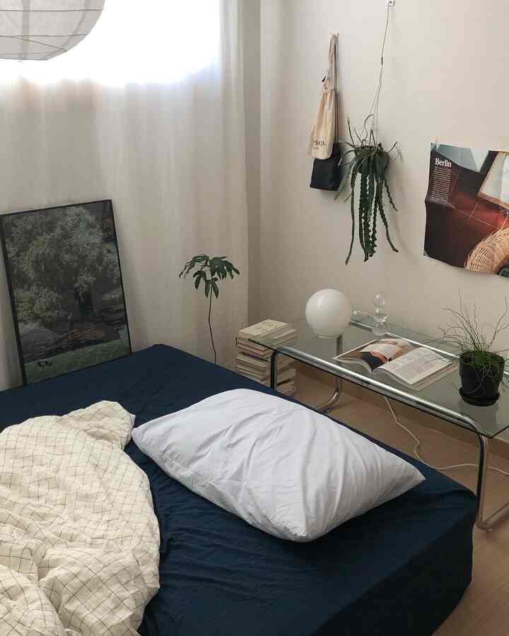 A bedroom in white and navy tones featuring a bed, side table, posters, and plants creating a natural and calm atmosphere