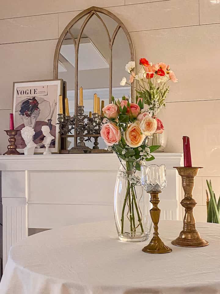 Beige-toned living room mantel with vintage decor items, featuring a vase of flowers and candle holders in a cozy setting