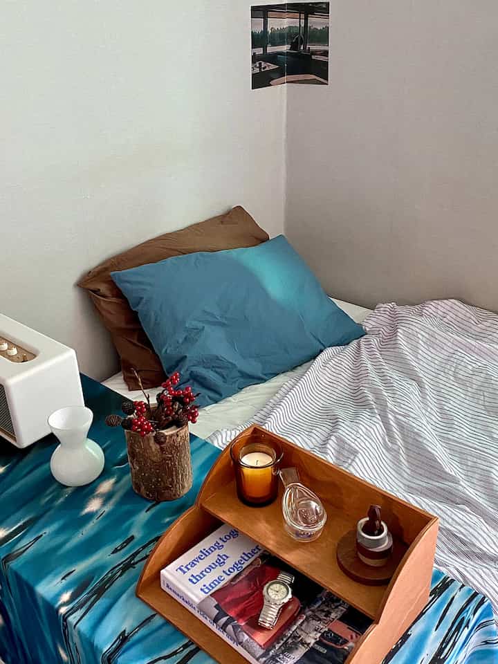 ブルーとブラウンの木目調が調和するワンルーム寝室、ベッドとサイドテーブルに小物が配置された落ち着いた空間