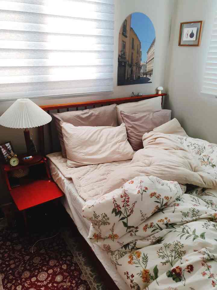 ナチュラルカラーとウッドトーンが調和したアットホームな寝室、花柄寝具とナチュラルコンビブラインドが配された空間