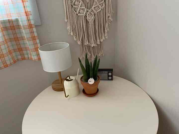 ベージュトーンの寝室コーナー、丸テーブルにスツーキーの植物とランプが配置された雰囲気のあるリモートワークスペース