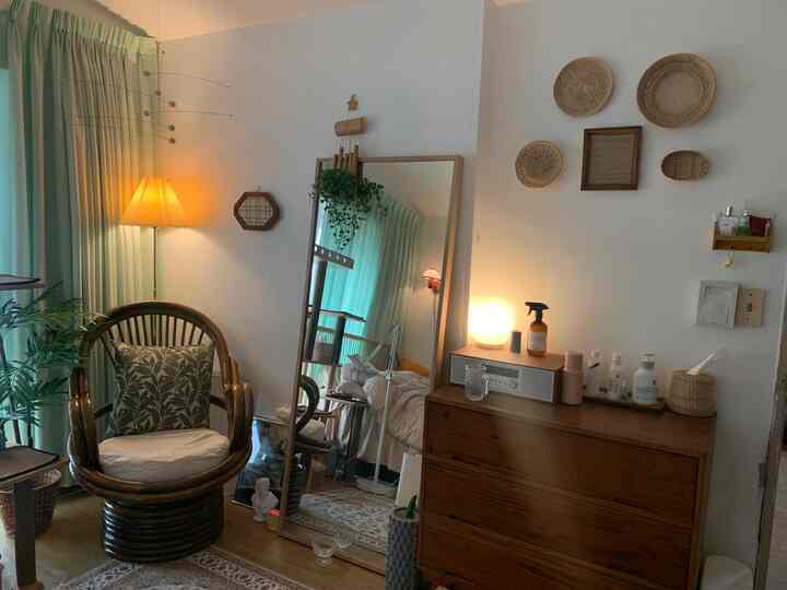 Cozy bedroom featuring mint curtains, wooden dresser, rattan chair, and warm lighting