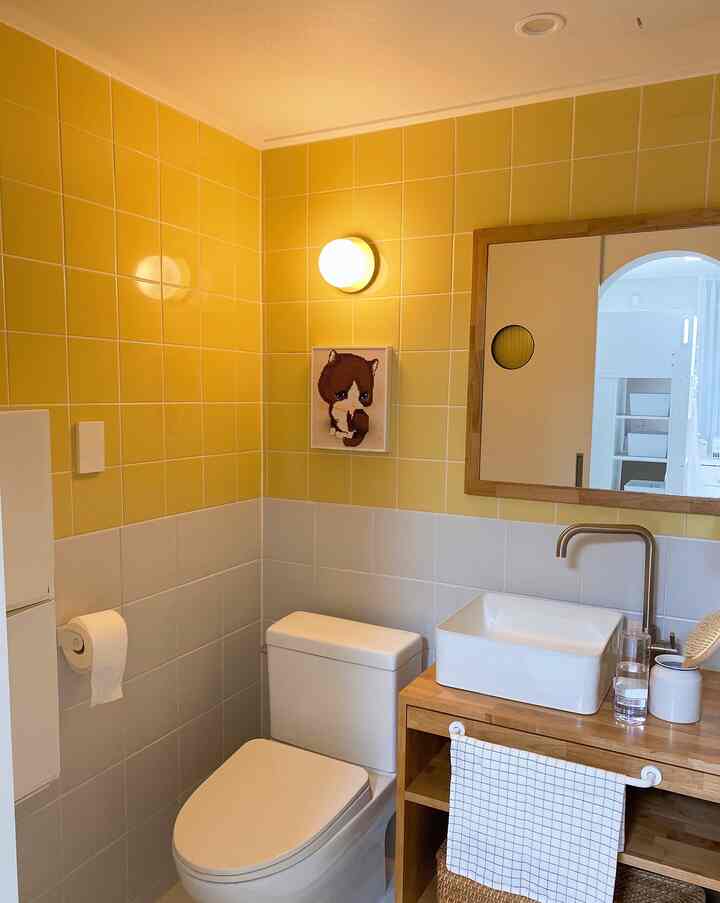 Bathroom with bright yellow and white tiles, wood tone vanity, and a cute cat picture frame creating a cozy atmosphere