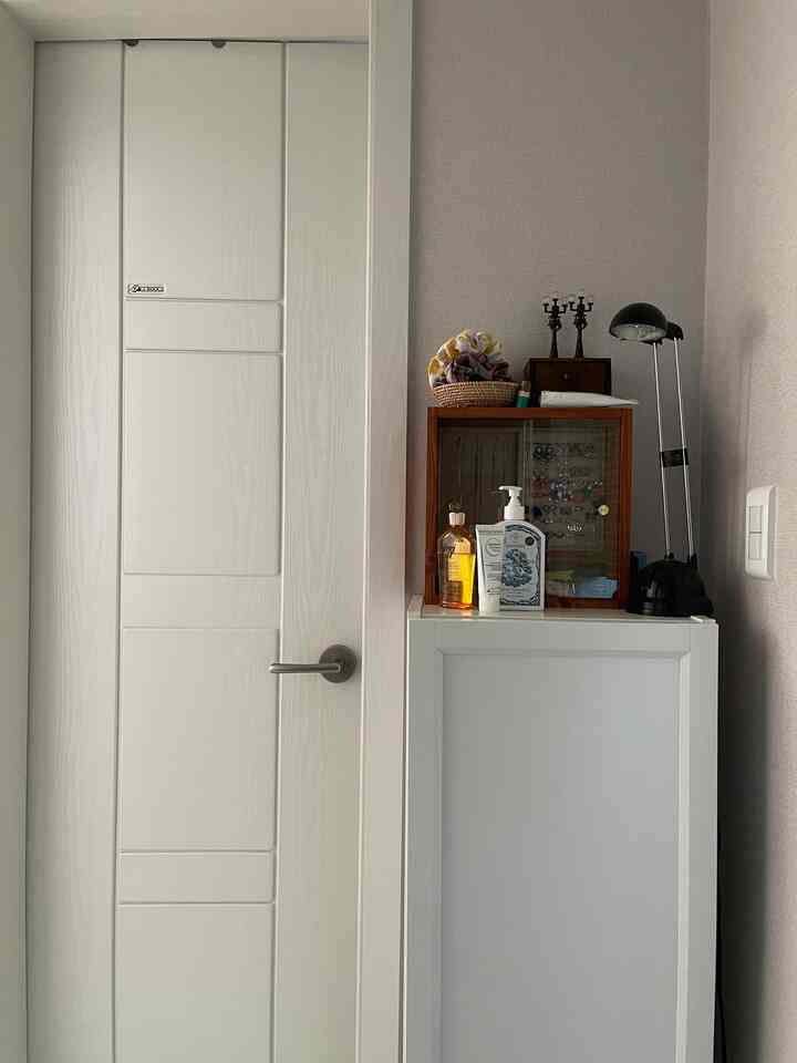 Clean space by the bathroom entrance featuring white storage cabinet and natural wood-tone accessories
