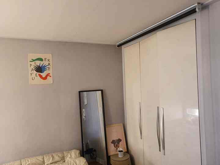 Natural tone small living room featuring a cream sofa, large white wardrobe, full-length mirror, and colorful wall poster with a simple ambiance