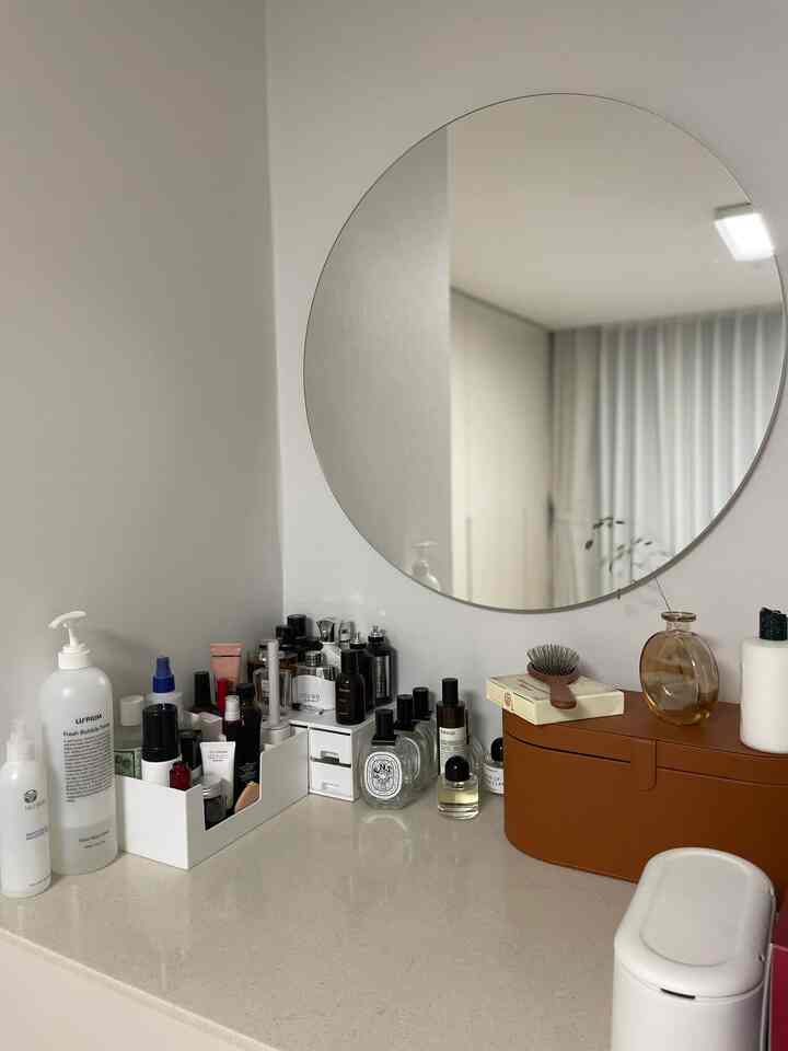 White and modern styled vanity featuring a large round mirror and neatly arranged cosmetics creating a clean space