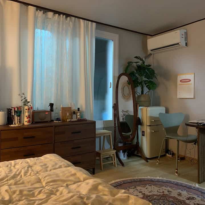 ナチュラルな木目調とホワイトが調和した一人暮らしの寝室、レトロ冷蔵庫と全身鏡が配置された雰囲気のある空間