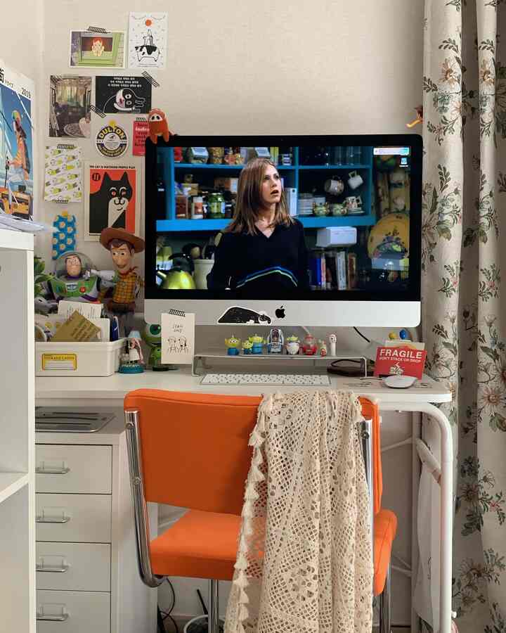 ホワイトトーンの壁とオレンジ色の椅子が調和した一人用ホームオフィス空間、玩具やウォールデコが温かみのある雰囲気を演出。