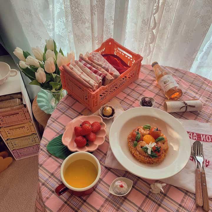 Cozy home cafe space featuring food, tea cup, and organized folding box on pink tablecloth