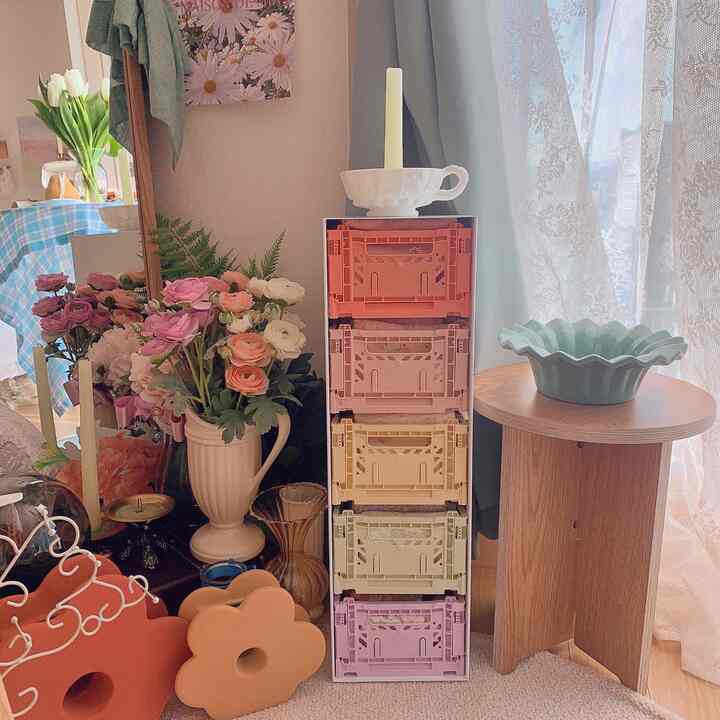 Pastel-toned apartment corner featuring colorful folding boxes, vases, and a wooden side table with a natural, cozy atmosphere