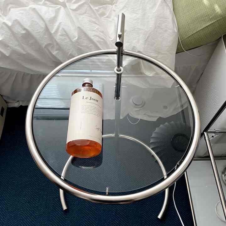 白い寝具とシルバーのメタルフレームのサイドテーブルが置かれた寝室、ダークブルーのラグの上にボトルがあるモダンな空間