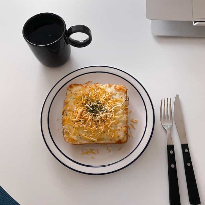 白いテーブルの上に黒いマグカップとチーズトーストが置かれた清潔感のあるおうちカフェ